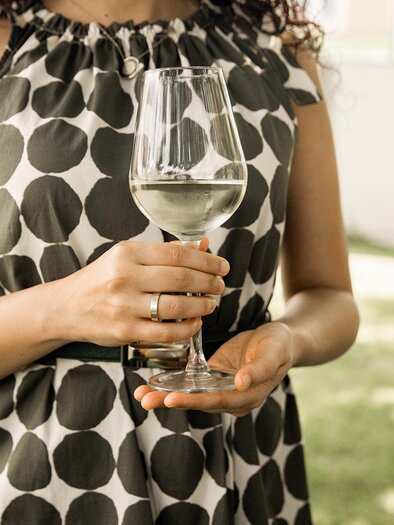 Eine Frau hält ein Glas Wasser in der Hand. Sie trägt ein gepunktetes Kleid und steht im Freien. | © TV Südsteiermark - achromaticphotography
