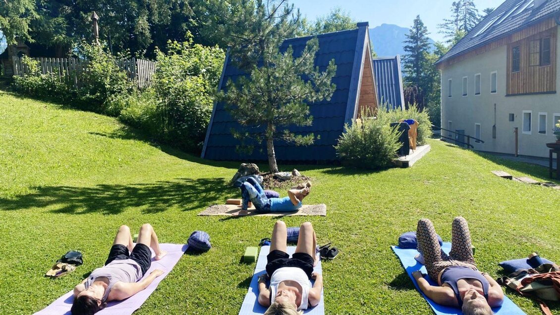 <p>Kursteilnehmerinnen von Yoga mit Kiki liegen auf Yogamatten im Freien. Im Hintergrund ist die grüne Landschaft des Ausseerlandes zu sehen.</p> | © Yoga mit Kiki