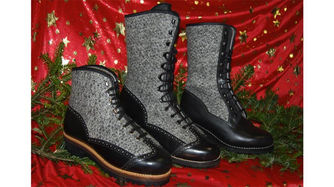 Drei stilvolle Stiefel aus grauem Wollmaterial und schwarzem Leder liegen auf einem roten, mit goldenen Sternen geschmückten Hintergrund. Sie sind ideal für kaltes Wetter und kombinieren Komfort mit eleganter Optik. | © Sonja Grill