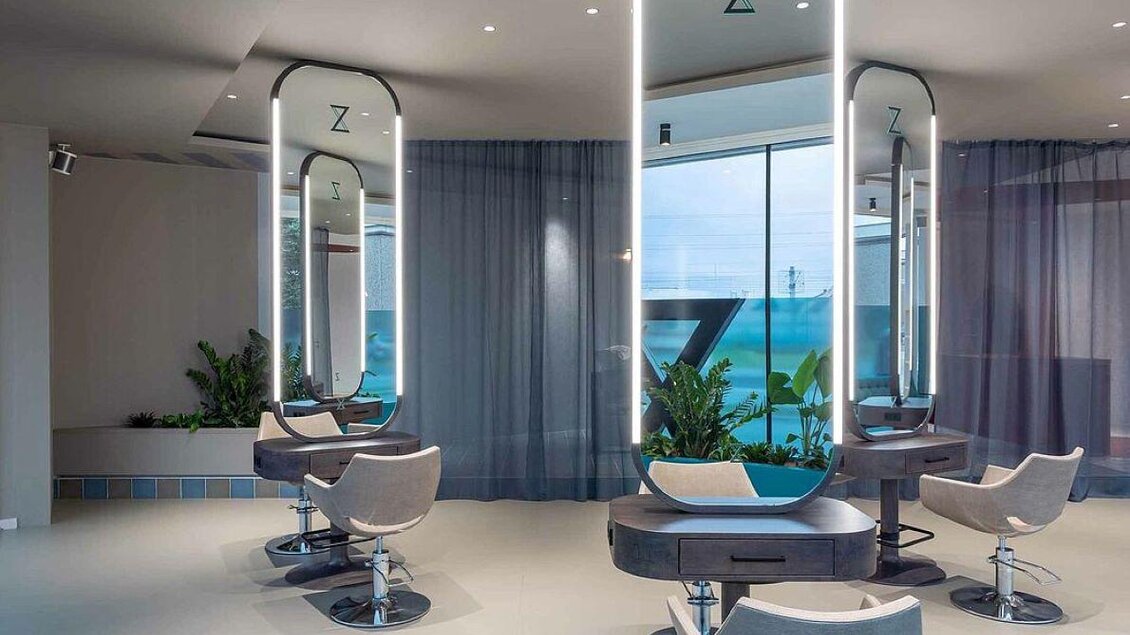Ein modernes Friseurstudio mit eleganten Arbeitsplätzen und großen Spiegeln. Die Fenster bieten einen Blick auf das Meer und sind umgeben von Pflanzen. | © Zeitgeist Frisiersalon