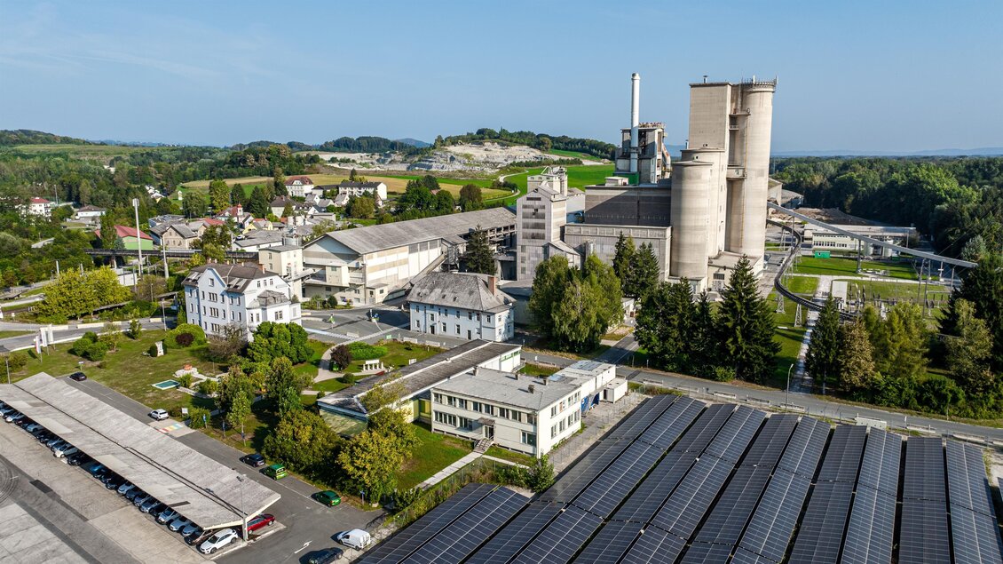 Eine moderne Industrieanlage umgeben von Grünflächen und Wohngebäuden. Im Vordergrund sind Solarpaneele zu sehen. | © Robert Sommerauer