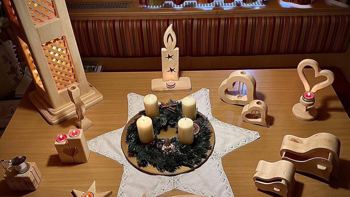 Eine festliche Tischdekoration mit Holzkerzenhaltern und einer Weihnachtskranz. In der Mitte stehen vier Kerzen auf einem Stern aus Holz. | © Zirben Toni
