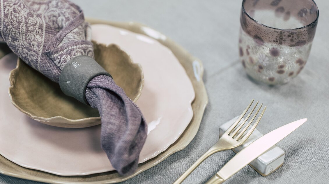 Ein stilvoll gedeckter Tisch mit rosa Tellern und einem dekorativen Serviette. Neben dem Geschirr steht ein elegantes Glas. | © vulkanland.at/bergmann