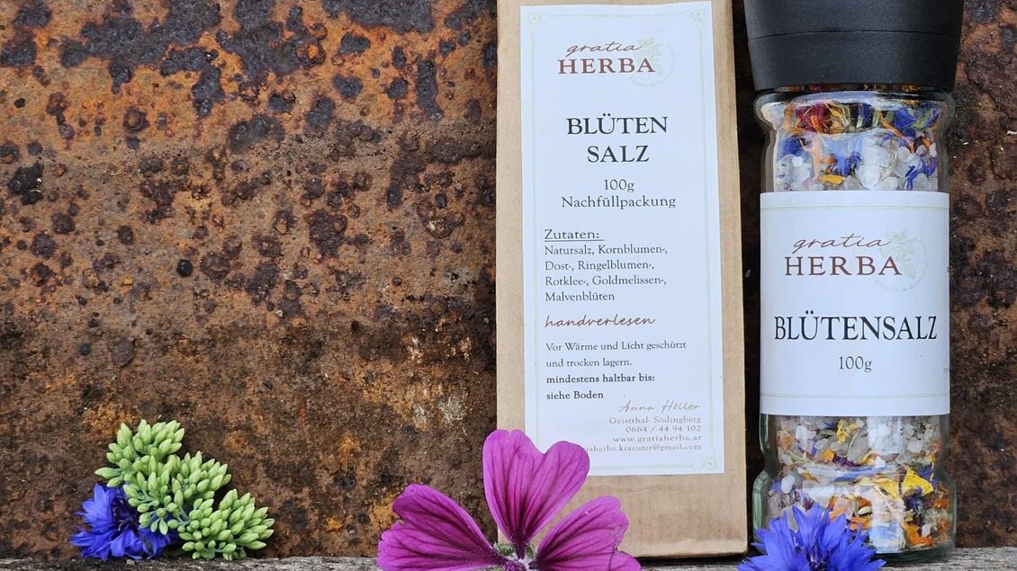 Verpackung und Glasbehälter mit Blütensalz von Gratia HERBA, umgeben von bunten Wildblumen auf rustikalem Hintergrund in Geistthal-Södingberg.  | © Anna Höller