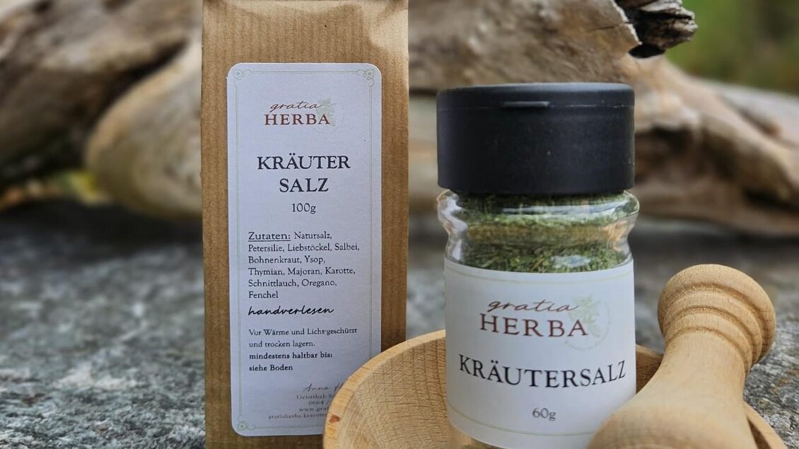 Verpackung und Glasbehälter mit Kräutersalz von Gratia HERBA, zusammen mit einer Holzschale und einem Stößel, auf einem Naturhintergrund in Geistthal-Södingberg.  | © Anna Höller