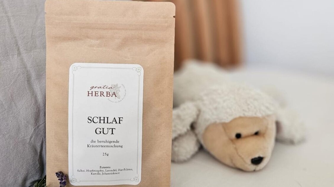 Tüte mit 'Schlaf Gut' Kräutertee von gratia HERBA auf einem Bett, neben einem Stoffbären und einem Zweig Rosmarin. | © Anna Höller