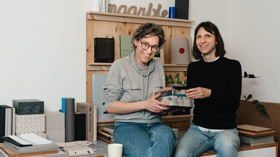 Die beiden Inhaberinnen von maarble sitzen mit einem handgefertigten Buch in ihrer Buchbinderei in Graz. | © Bernd Grosseck