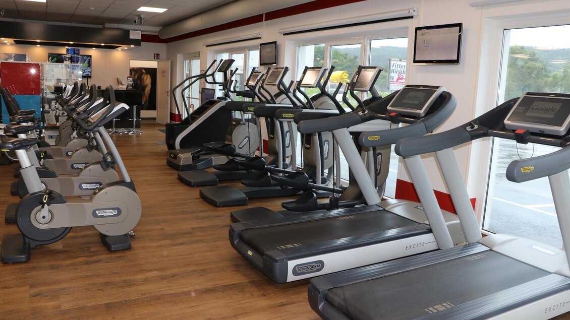 Ein moderner Fitnessraum mit verschiedenen Cardio-Geräten. Die große Fensterfront sorgt für viel Tageslicht. | © Daniel Schreiber