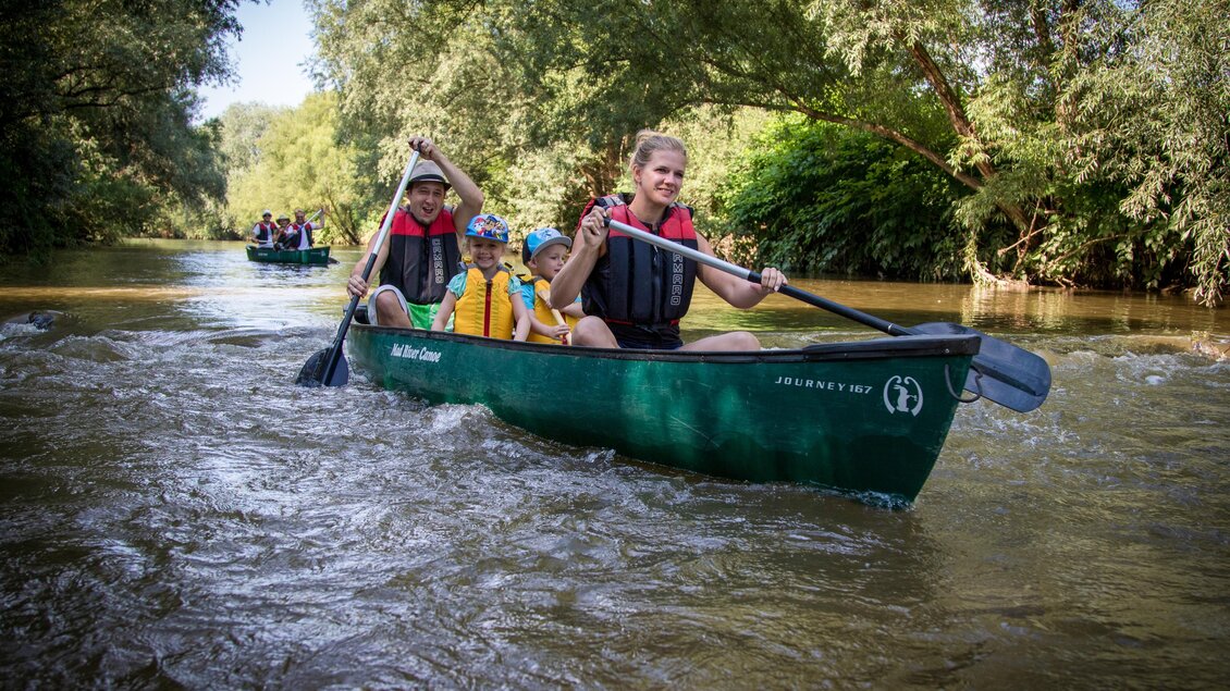 Eine Gruppe von Menschen paddelt in Kanus auf einem ruhigen Fluss. Umgeben von üppigem Grün und Bäumen genießen sie die Natur. | © RM SW GmbH | webquartier.at