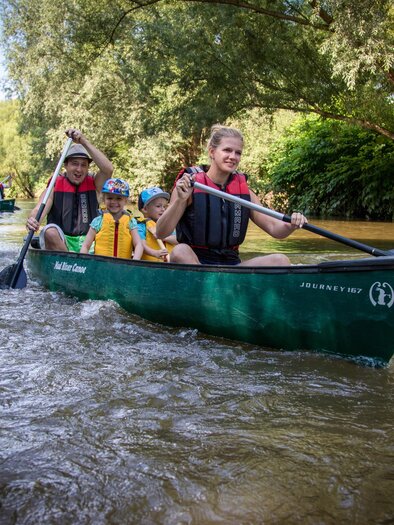 Eine Gruppe von Menschen paddelt in Kanus auf einem ruhigen Fluss. Umgeben von üppigem Grün und Bäumen genießen sie die Natur. | © RM SW GmbH | webquartier.at