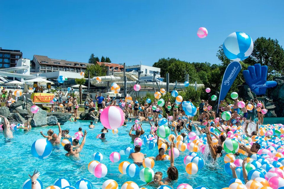 Ein lebendiger Pool voller Menschen, die mit bunten Wasserbällen spielen. Im Hintergrund sind sonnige Liegen und eine klare Himmel zu sehen. | © Thermenresort Loipersdorf