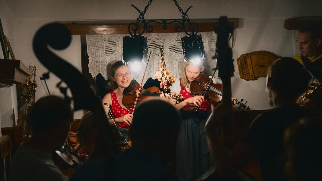 Eine Gruppe von Musikern spielt in einem gemütlichen Raum. Die Musikerinnen mit Geigen stehen im Licht und schaffen eine feierliche Stimmung.
