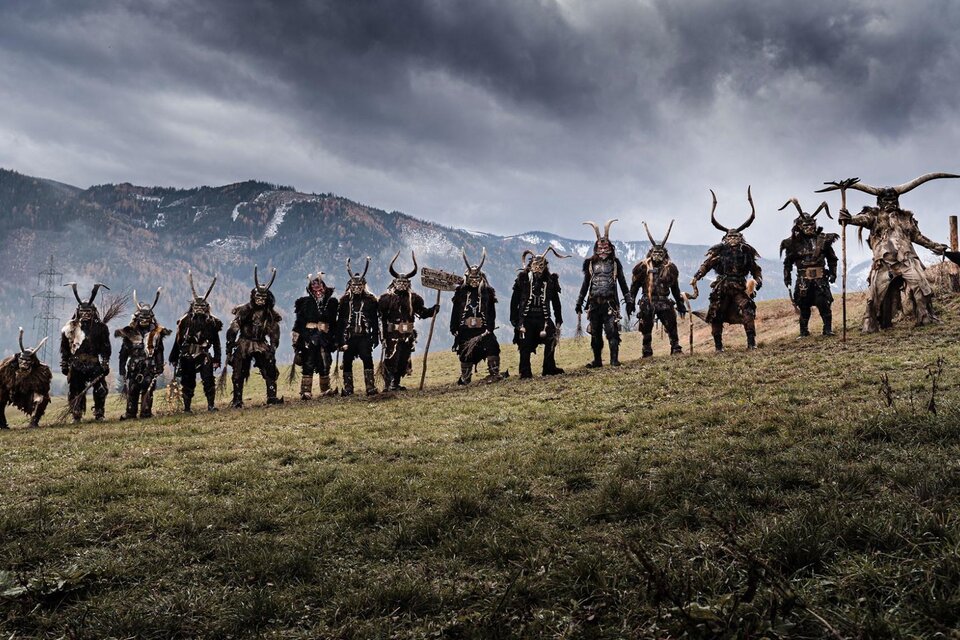 Eine Gruppe von mystisch gekleideten Figuren steht auf einer Wiese vor Bergen. Das Wetter ist bewölkt und die Szenerie hat eine dramatische Atmosphäre. | © Ehrenfels Pass Kammern