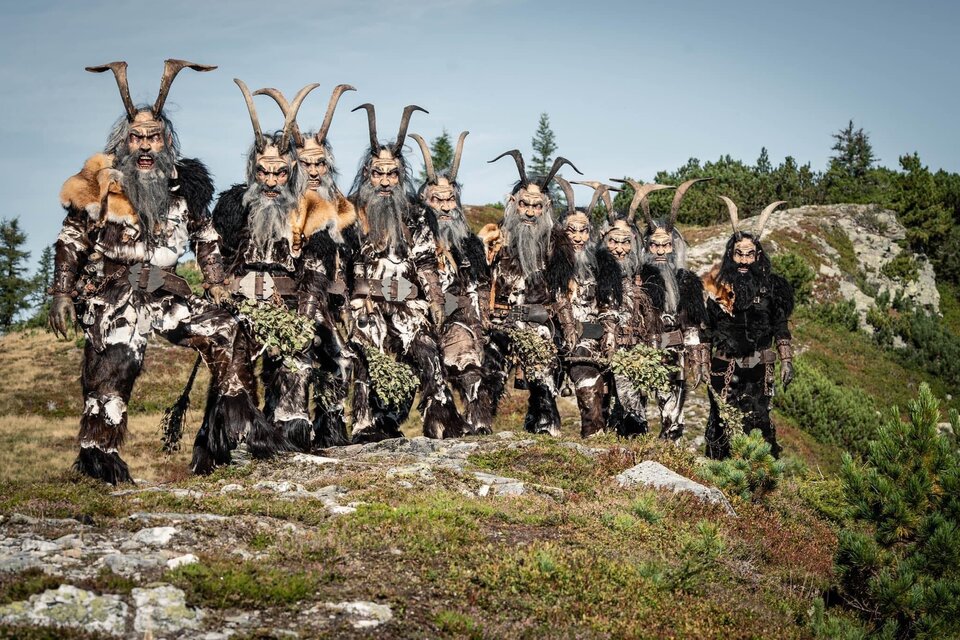 Eine Gruppe von Menschen in beeindruckenden Kostümen mit Hörnern steht auf einem Hügel. Der Hintergrund zeigt eine natürliche Landschaft mit Bäumen und einem klaren Himmel. | © Krampusriege Mautern