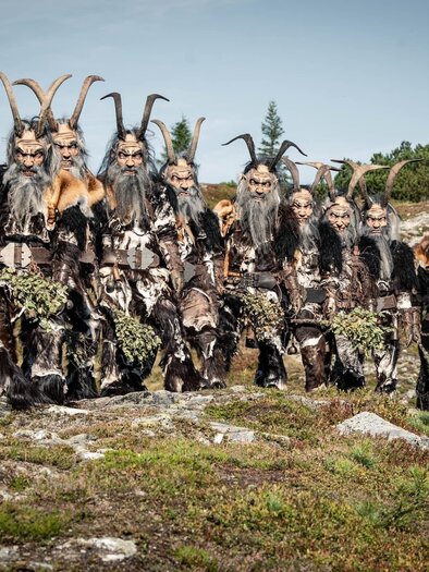 Eine Gruppe von Menschen in beeindruckenden Kostümen mit Hörnern steht auf einem Hügel. Der Hintergrund zeigt eine natürliche Landschaft mit Bäumen und einem klaren Himmel. | © Krampusriege Mautern