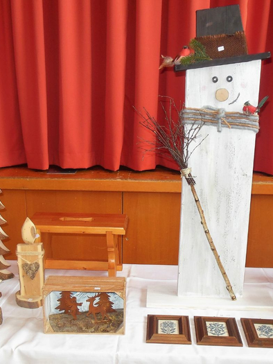 Eine festliche Dekoration mit handgemachten Holzfiguren, darunter Weihnachtsbäume und eine Schneemannfigur. Auf dem Tisch sind auch verschiedene Kerzen und Laternen zu sehen. | © Engelbert Haim