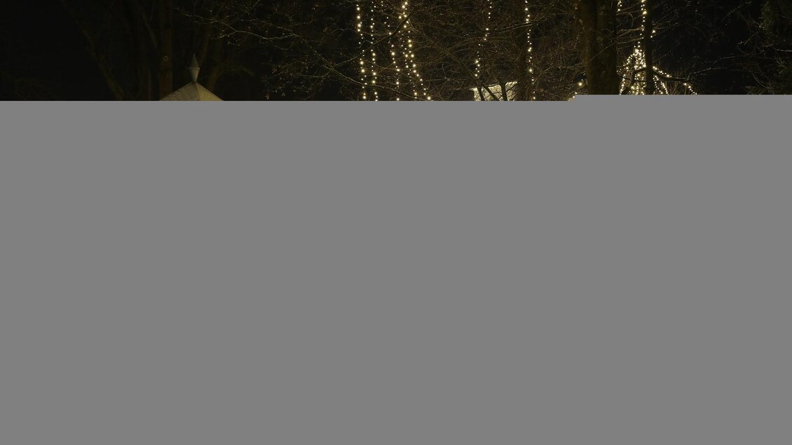 Ein festlich beleuchteter Platz mit einem Pavillon und geschmückten Weihnachtsbäumen. Menschen spazieren durch die verschneite Umgebung in der Nacht. | © Stadtgemeinde Trofaiach