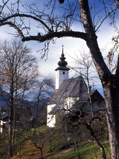 Ein roter Weihnachtsbaumkugel hängt an einem schneebedeckten Baum. Im Hintergrund leuchten festliche Lichter eines Weihnachtsmarktes. | © Tourismusverband Bad Aussee