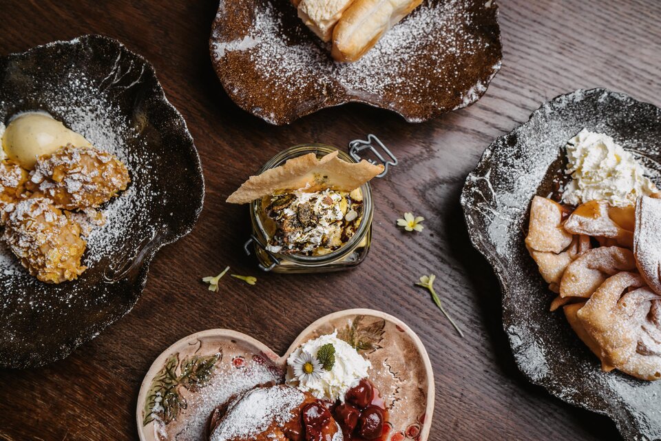 Ein liebevoll angerichtetes Dessert-Arrangement auf rustikalen Tellern. Die verschiedenen Süßspeisen sind mit Puderzucker bestreut und verziert. | © Michaela Lorber