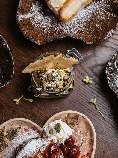 Ein liebevoll angerichtetes Dessert-Arrangement auf rustikalen Tellern. Die verschiedenen Süßspeisen sind mit Puderzucker bestreut und verziert. | © Michaela Lorber
