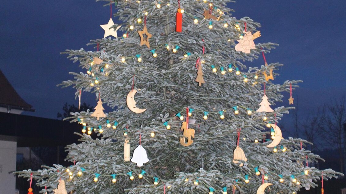 Ein festlich geschmückter Weihnachtsbaum mit bunten Lichtern und Holzornamenten. Der Baum steht vor einem dunklen Himmel. | © Gemeinde Bad Loipersdorf