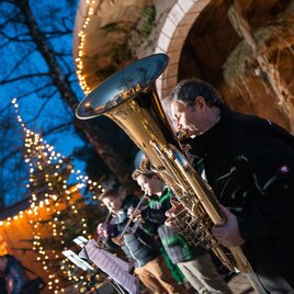 Drei Blasmusiker spielen mit Tuba und Trompeten vor einer beleuchteten Weihnachtskrippe am Weihnachtsmarkt in Laßnitzhöhe. | © TV Region Graz-Ulf Thausing