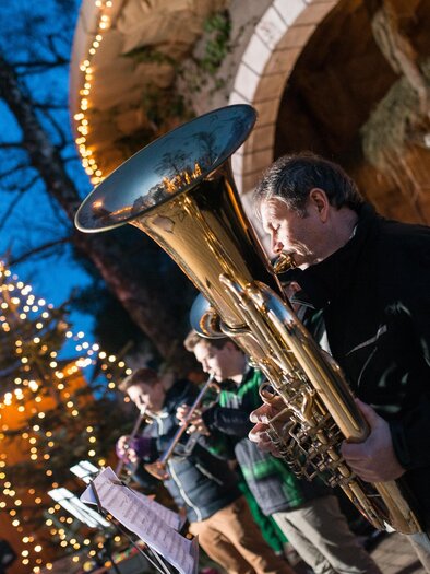 Drei Blasmusiker spielen mit Tuba und Trompeten vor einer beleuchteten Weihnachtskrippe am Weihnachtsmarkt in Laßnitzhöhe. | © TV Region Graz-Ulf Thausing