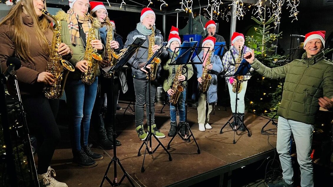 Eine Gruppe von Musikern spielt Saxophon in Weihnachtsmützen. Es ist festlich dekoriert mit Lichtern im Hintergrund. | © Klara Tischler
