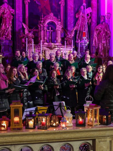 A choir sings in a festively illuminated church. In the foreground, lanterns and a decorative stage can be seen. | © Foto De Monte