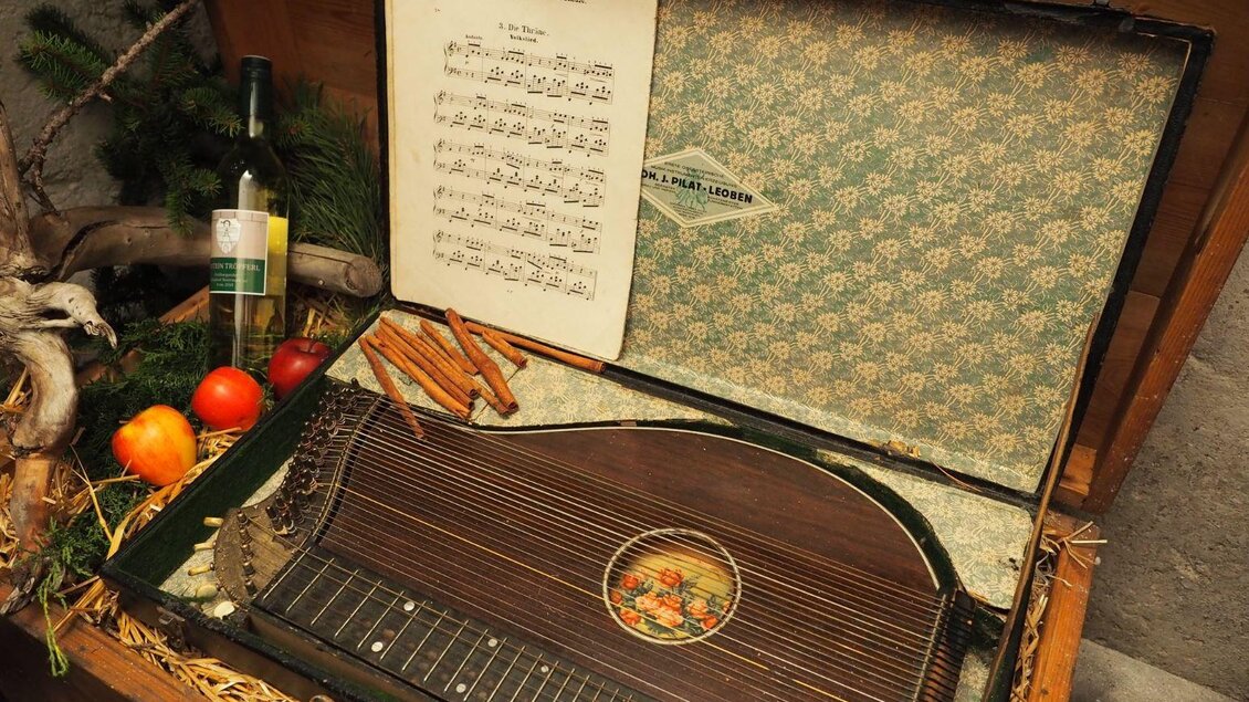 Eine schöne Zithermusik mit Notenblatt in einer dekorativen Kiste. Der Koffer enthält auch Früchte und eine Flasche. | © Wolfgang Gaube
