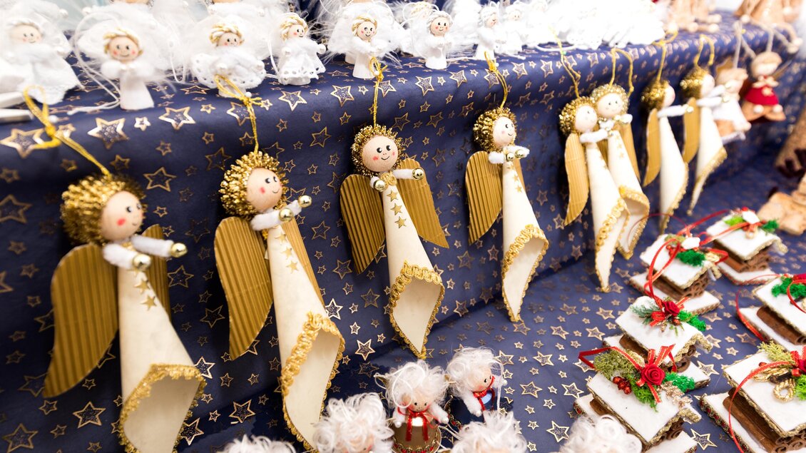 Eine festliche Auswahl an handgefertigten Engel-Ornamenten hängt von einer blauen Decke mit goldenen Sternen. Im Vordergrund sind dekorierte Lebkuchen zu sehen. | © TV Region Graz-Harry Schiffer