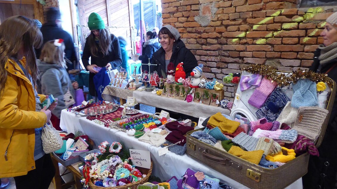 Wollartikel in allen Varianten werden angeboten beim Adventmarkt Taggerhof in Kainbach b. Graz. Rechts daneben ist das Eingangstor, es fällt Tageslicht ins Innere.  | © Manfred Schöninger
