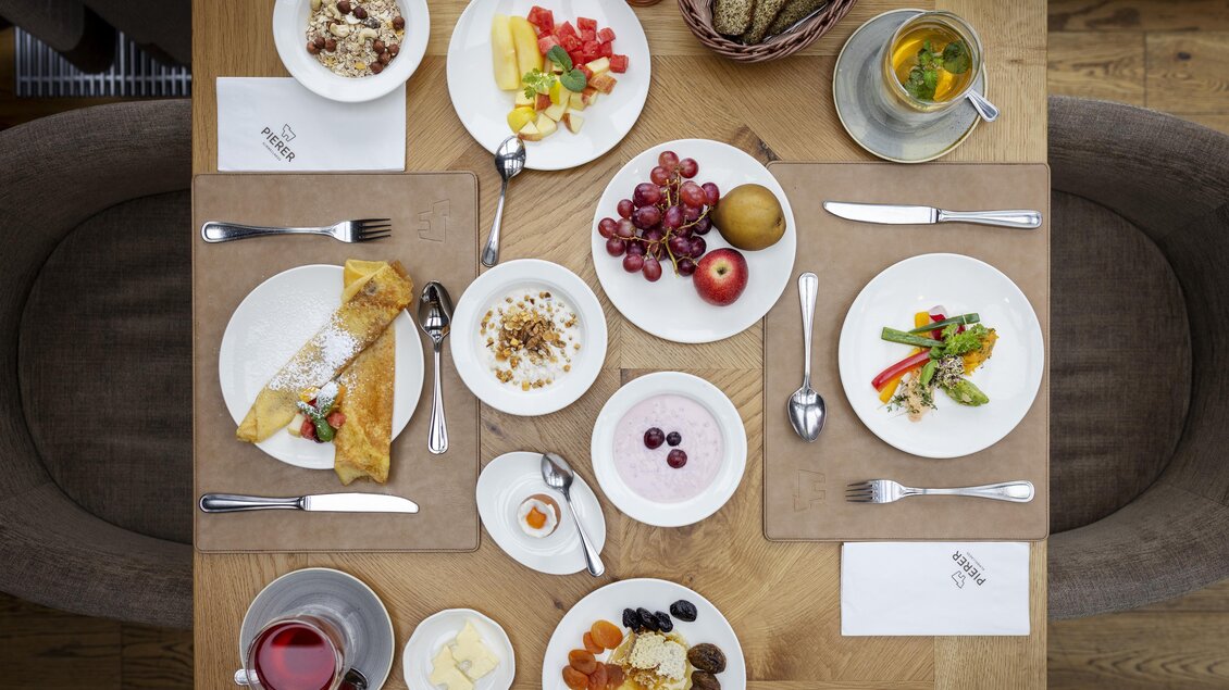 Ein reichhaltiges Frühstück mit verschiedenen Gerichten, einschließlich Obst, Joghurt und Omelett. Der Tisch ist schön gedeckt und lädt zum Genießen ein. | © Almwellness Hotel Pierer