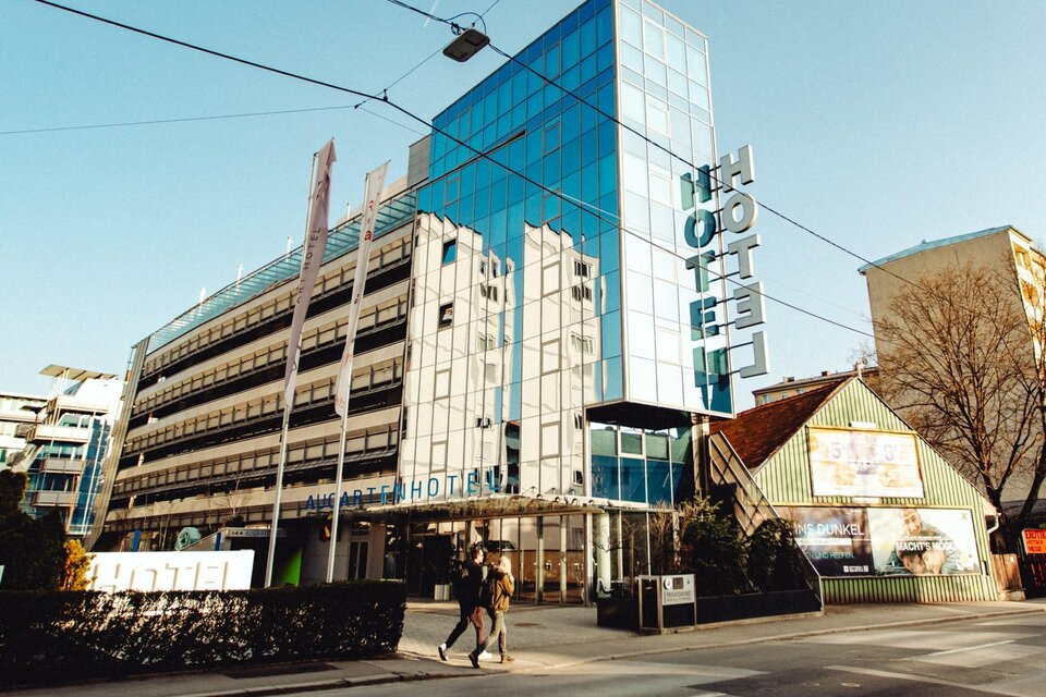 Moderne Glasfassade des Augarten Art Hotels an einer Straße in Graz mit Eingangsbereich und Hotelschriftzug. | © Mikhail Kyrillos