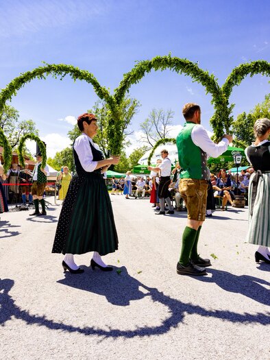 Folk dance group in traditional costumes dances with green arches at the Styrian Roas in St. Bartholomä in front of an audience. | © Region Graz-Harry Schiffer