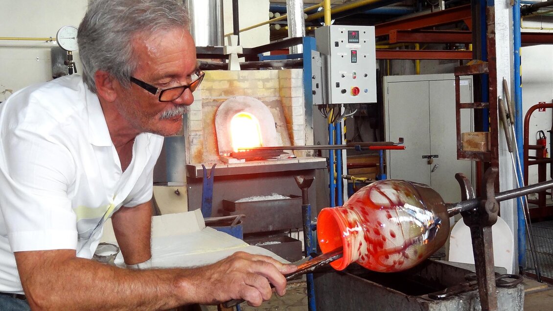 Glaskünstler Heinz Strasser formt an der Glasmacherpfeife ein glühendes, mundgeblasenes Glas in der Werkstatt. | © GlasMuseum Bärnbach