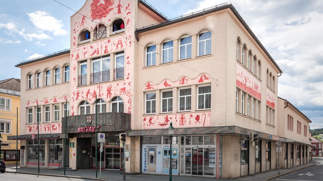 Ein historisches Gebäude mit einer kunstvollen rosa Fassade und großen Fenstern. Es befindet sich an einer Straßenecke und hat eine markante Architektur. | © Lipizzanerheimat-DieAbbilderei