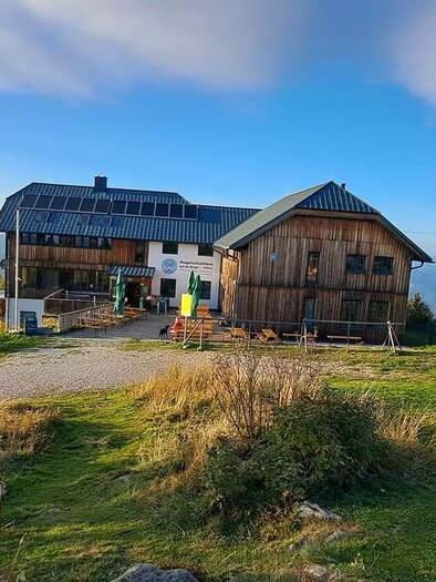 A cabin in the mountains with a beautiful view. The surroundings are green and the sky is clear and blue. | © Weißmüller