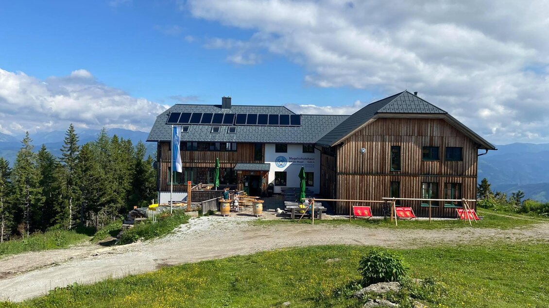 Ein rustikales Berghaus mit Solarpanelen in einer malerischen Landschaft. Umgeben von grüner Wiese und Bäumen unter einem blauen Himmel. | © TVB Erzberg-Leoben