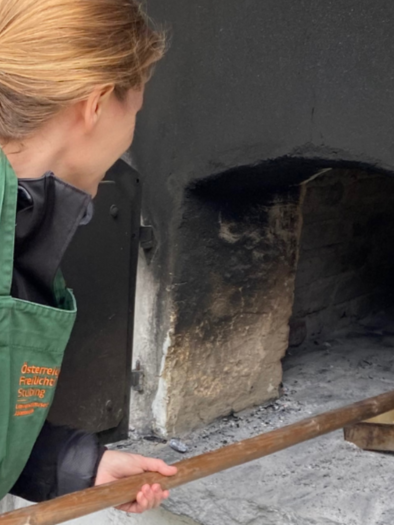 <p>A woman pushes bread dough with a wooden peel into a historical bread baking oven at the Austrian Open-air Museum Stübing.</p> | © ÖFM