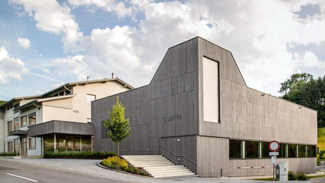 Modernes Schulgebäude in Nestelbach bei Graz mit grauer Holzfassade, großen Fenstern und Treppenaufgang. | © Andrea Filipancic
