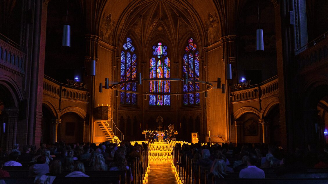 Kircheninnenraum der Herz-Jesu-Kirche in Graz mit Publikum und Bühne eines Candlelight-Konzerts im Kerzenlicht. | © feverup.com
