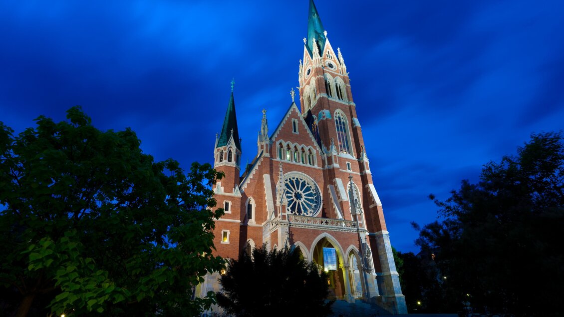 Eine beeindruckende Kirche mit hohen Türmen und einem großen Rosenfenster. Der Himmel ist dunkelblau und verleiht der Szene eine besondere Stimmung. | © Graz Tourismus-Harry Schiffer