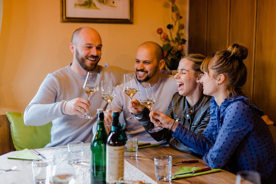 Eine Gruppe von Freunden sitzt an einem Tisch und hebt ihre Gläser zum Anstoßen. Sie lachen und genießen einen fröhlichen Moment zusammen. | © Ratscher Landhaus