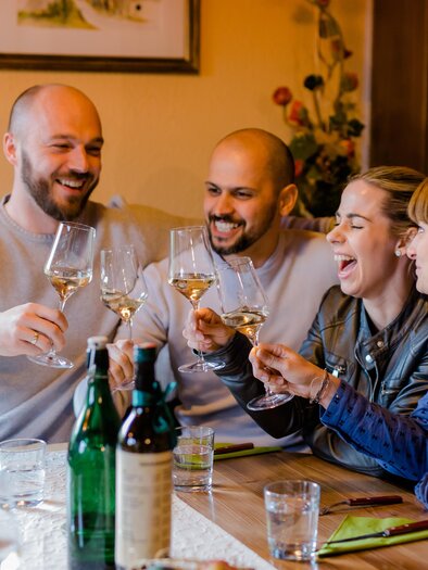 Eine Gruppe von Freunden sitzt an einem Tisch und hebt ihre Gläser zum Anstoßen. Sie lachen und genießen einen fröhlichen Moment zusammen. | © Ratscher Landhaus