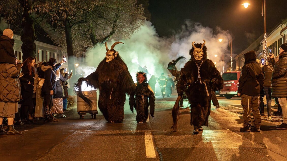 Eine nächtliche Parade mit Menschen in auffälligen Kostümen. Es gibt rauchige Effekte und Zuschauer am Straßenrand. | © Foto de Monte Mureck