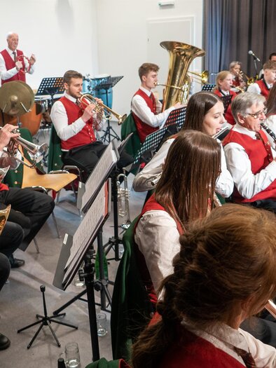 Eine Blaskapelle spielt in einem Saal. Die Musiker tragen rote Westen und spielen verschiedene Blasinstrumente. | © echtzeit-tv, Stefan Lendl.