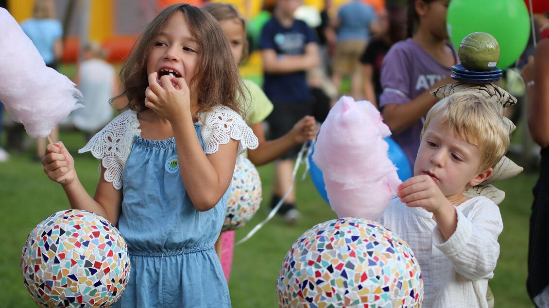 Ein fröhliches Kinderfest im Freien mit Kindern, die bunte Luftballons halten. Zwei Kinder genießen Zuckerwatte und haben große, gemusterte Bälle in der Hand. | © Barmherzige Brüder