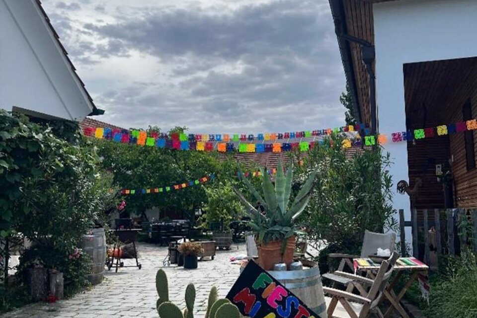 Ein einladender Außenbereich mit bunten Papiergirlanden und Pflanzen. Die gemütliche Atmosphäre wird durch Holzstühle und dekorative Elemente verstärkt. | © Familie Scharl