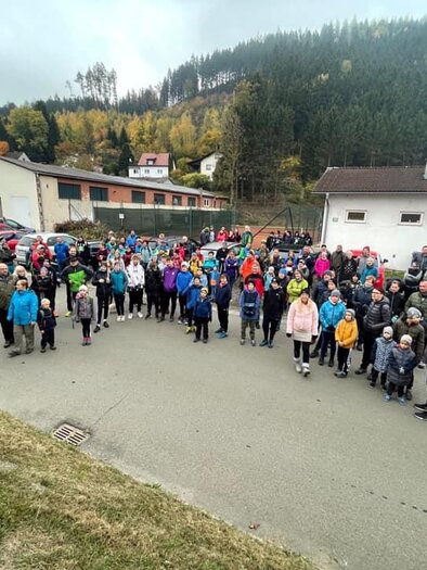 Eine große Gruppe von Menschen versammelt sich draußen auf einem Parkplatz. Sie tragen bunte Kleidung und scheinen an einem Event oder einer Veranstaltung teilzunehmen. | © ATUS Niklasdorf